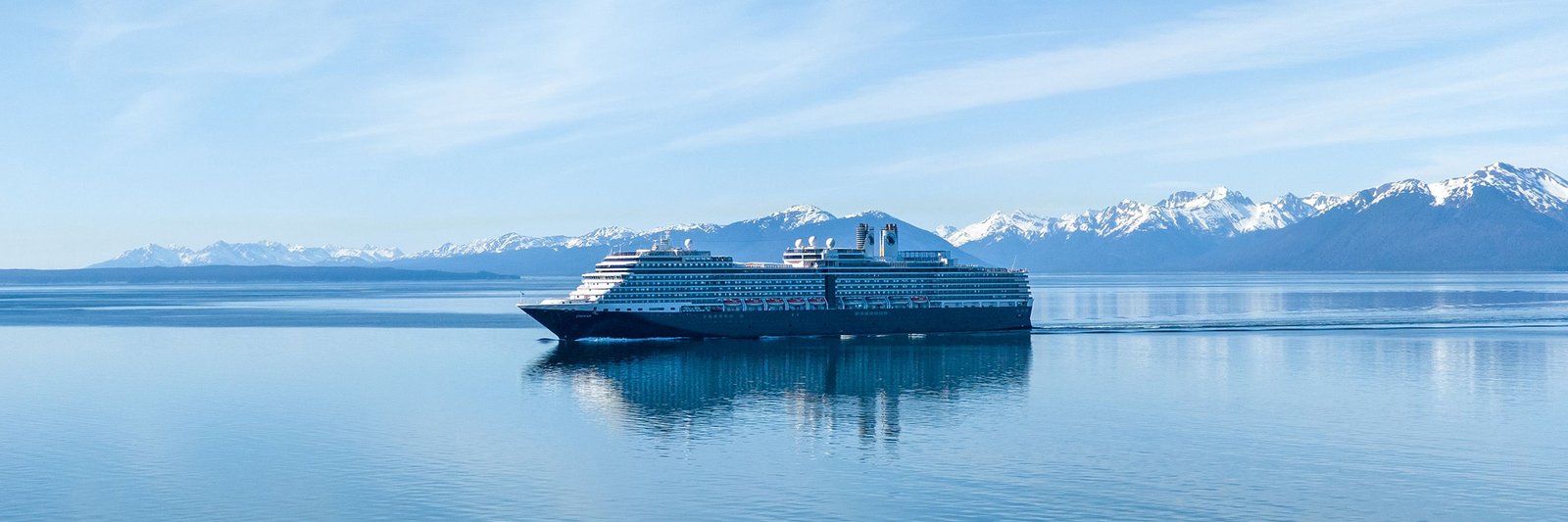 Cruise ship on calm water below a snow-capped mountain range